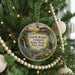 A circular ornament hanging on a Christmas tree, featuring a scenic landscape with a waterfall, path, and flowers.