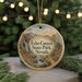 A round ornament with a painting of Echo Canyon State Park in Nevada, featuring a waterfall and mountains, is displayed on a table with pine branches and twinkling lights in the background.