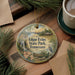 A decorative ornament with a scenic image of Edgar Evans State Park, Tennessee, featuring a waterfall, cabin, and bird, is displayed on a wooden surface alongside a cup of coffee and some pine branches.