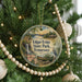 A round ornament hanging on a Christmas tree, featuring a scenic landscape with a waterfall, a bird, and a canoe.