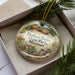A decorative ornament in a box, featuring an illustration of a scenic landscape with a bridge and rocks, along with the text "Elephant Rocks State Park, Missouri".