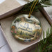 A decorative ornament in a box, featuring a scenic landscape with a deer, trees, and a waterfall, along with the text "Elk State Park, Pennsylvania".