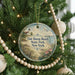 A round ornament hanging on a Christmas tree, featuring a lighthouse and a beach scene.