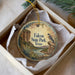 A decorative ornament in a box, featuring a bird and a landscape scene with mountains and a river.