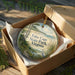 A decorative ornament in a brown box, featuring a scenic landscape with a bird and trees, with the text "False Cape State Park, Virginia" printed on it.