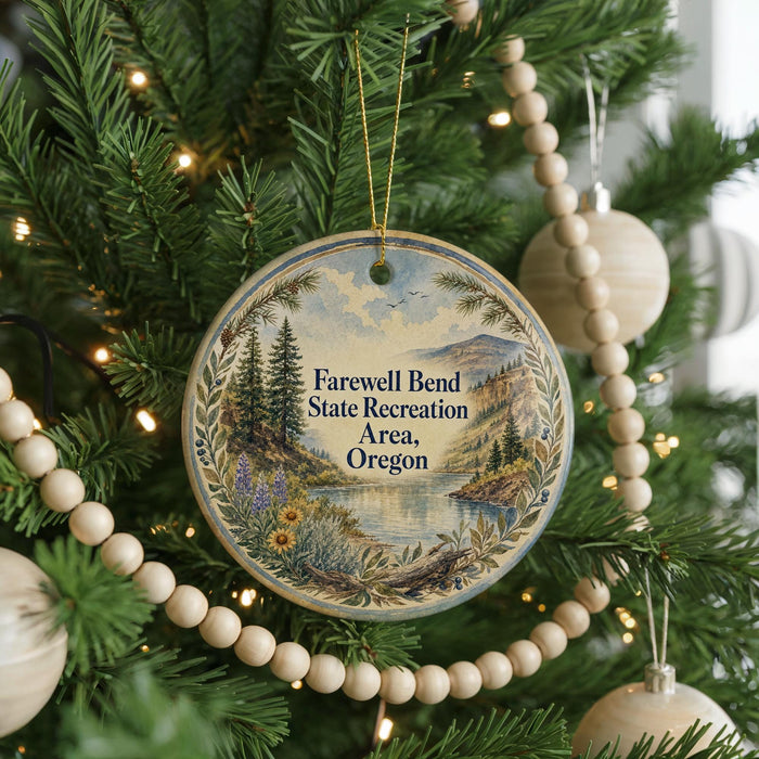A round ornament hanging on a Christmas tree, featuring a scenic landscape with mountains, trees, and a lake.