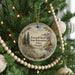 A round ornament hanging on a Christmas tree, featuring a scenic landscape with mountains, trees, and a lake.