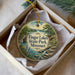 A decorative ornament in a box, featuring a scenic landscape with a river, trees, and a waterfall.