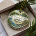 A decorative ornament in a box, featuring a scenic landscape with a lake and mountains.