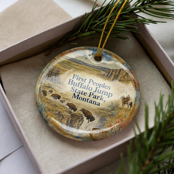 A decorative ornament in a box, featuring a scenic landscape with buffalo and mountains, along with text that reads "First Peoples Buffalo Jump State Park, Montana".