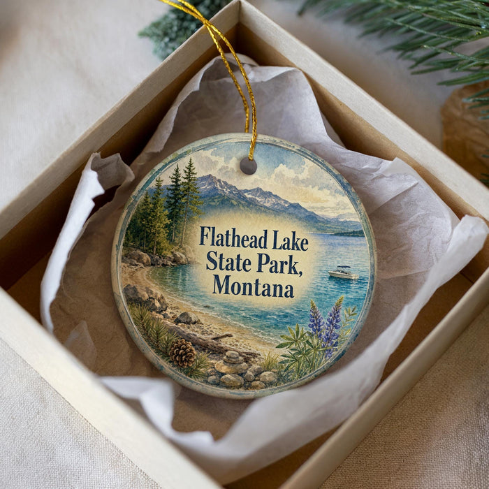 A decorative ornament in a box, featuring a scenic landscape with mountains, pine trees, and a lake.