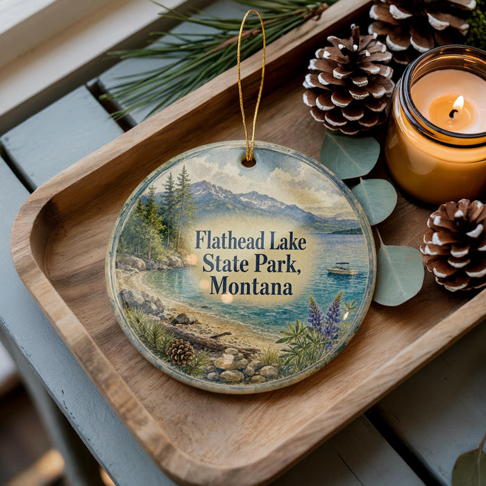 A decorative ornament featuring a scenic landscape of Flathead Lake State Park, Montana, with pine cones and a lit candle on a wooden tray.