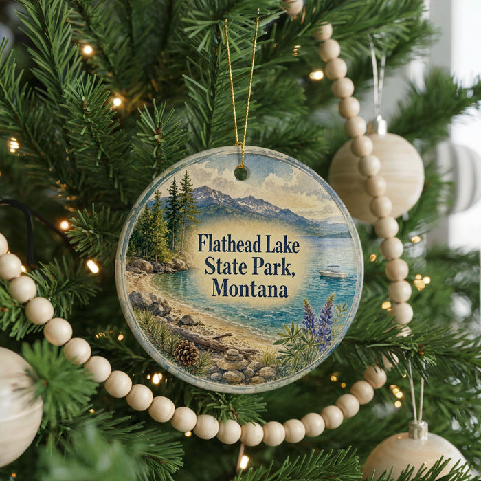 A round ornament hanging on a Christmas tree, featuring a scenic landscape of Flathead Lake State Park, Montana.