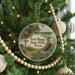 A round ornament hanging on a Christmas tree, featuring a scenic landscape with a windmill and a river.