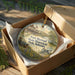 A round ornament in a box, featuring an illustration of Fort Hartsuff State Historical Park in Nebraska.