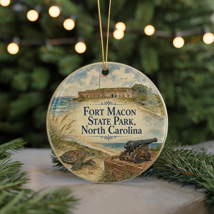 A round ornament featuring a painting of Fort Macon State Park in North Carolina, with a cannon and a turtle in the foreground.