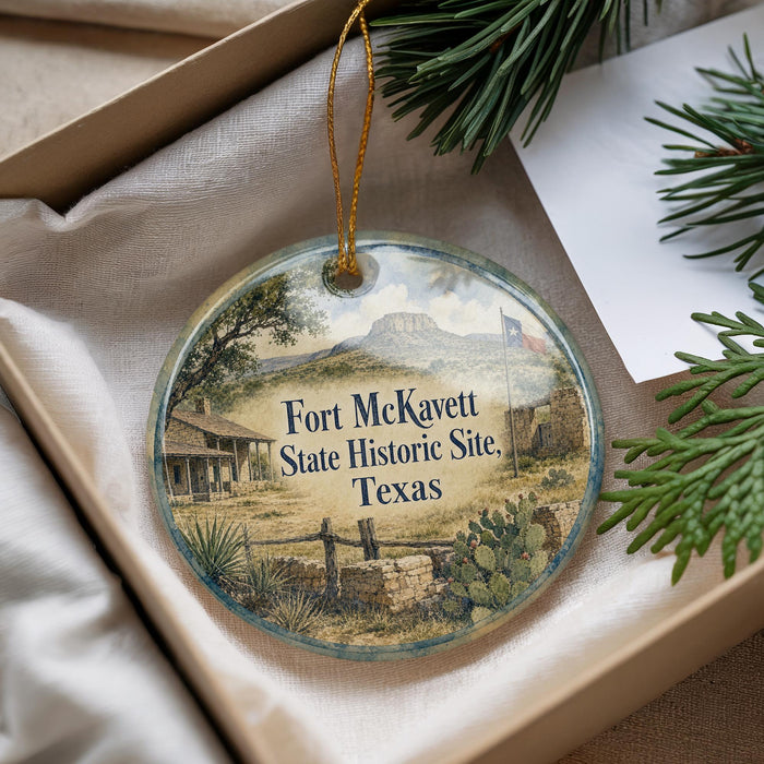 An oval ornament with a picture of Fort McKeett, a historic site in Texas, is displayed in a box with pine branches.