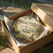 A circular ornament in a wooden box, featuring an illustration of Fort Phil Kearny, the State Historic Site in Wyoming.
