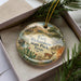 A decorative ornament in a box, featuring a scenic image of Fort Richardson State Park in Texas.
