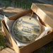 A round ornament in a box, featuring a scenic image of Fort WORDEN State Park in Washington.