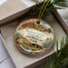 A decorative ornament in a box, featuring a scenic image of the Fremont Indian State Park and Museum in Utah.