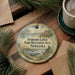 A round ornament with a scenic landscape of Fremont Lakes, Nebraska, hangs on a wooden surface, accompanied by pine branches and a cup of coffee.