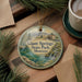 A decorative ornament featuring a scenic landscape of Giant Springs State Park, Montana, with a small house and waterfall in the background.