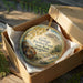 A decorative ornament in a wooden box, featuring a scenic landscape with mountains and a winding path.
