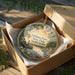 A decorative ornament in a brown box, featuring a scenic landscape with a river, trees, and a boat, along with the text "Givhan's Ferry State Park, South Carolina".