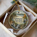 A decorative ornament in a box, featuring a scenic landscape with a lake, a house, and a bird, along with the text "Glimmerglass State Park, New York".