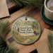A circular ornament with a scenic illustration of Good Earth State Park, South Dakota, featuring a bison, a cabin, and a waterfall.