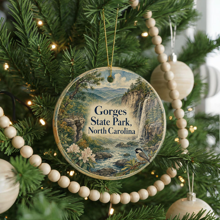 A round ornament hanging on a Christmas tree, featuring a scenic landscape with a waterfall and mountains.