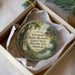 A circular ornament with a painting of a historic site, specifically the Governor Daniel Dunlin's grave, surrounded by a forest and a small cabin.