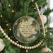 A round ornament hanging on a Christmas tree, featuring a scene of Daniel Dunlin's grave surrounded by trees and a house.