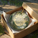 A round ornament in a wooden box, featuring a scenic landscape with a monument and a house, along with the text "Governor Daniel Dunklin's Grave State Historic Site, Missouri".