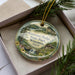 A decorative ornament in a box, featuring a scenic landscape of Governor Dodge State Park in Wisconsin.