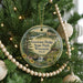 A circular ornament hanging on a Christmas tree, featuring a scenic landscape with a waterfall and pine trees.