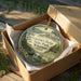 A decorative ornament in a wooden box, featuring a scenic landscape with a waterfall and forest.