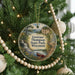 A circular ornament hanging on a Christmas tree, featuring a scenic landscape with a waterfall and a canoe.