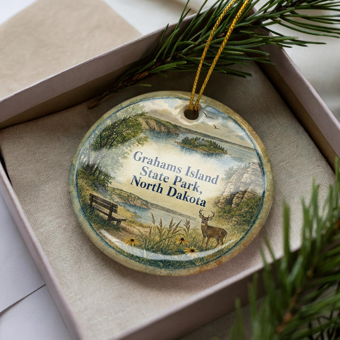 A decorative ornament featuring a scenic landscape of Grahams Island State Park in North Dakota, with a bench and a deer in the foreground.