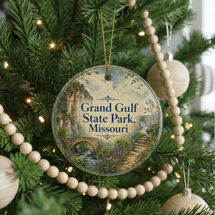 A round ornament hanging on a Christmas tree, featuring a scenic landscape with a bridge and a river.
