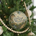 A round ornament hanging on a Christmas tree, featuring a scenic landscape with a bridge and a river.