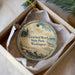A circular ornament with a beach scene and text, placed in a box with a white tissue paper lining.