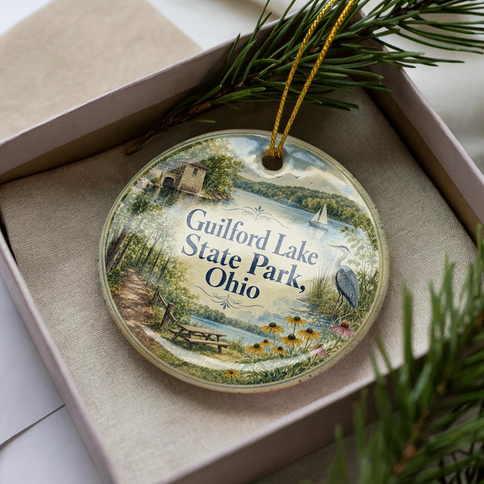 A decorative ornament in a box, featuring a scenic landscape with a lake, trees, and a bird, along with the text "Guilford Lake State Park, Ohio".