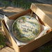 A decorative ornament in a box, featuring a scenic landscape with a lake, park, and a bird, along with the text "Guilford Lake State Park, Ohio".