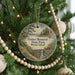 A round ornament hanging on a Christmas tree, featuring a scenic landscape with a bridge and a body of water.