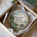 A decorative ornament in a white box, featuring a beach scene with birds, a turtle, and a palm tree.