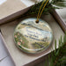 A decorative ornament in a box, featuring a beach scene with a lifeguard tower and a path leading to the beach.