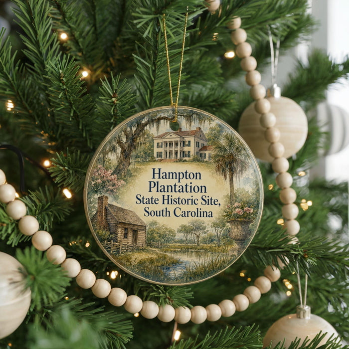 A round ornament hanging on a Christmas tree, featuring a painting of a historic plantation house surrounded by trees and a pond.