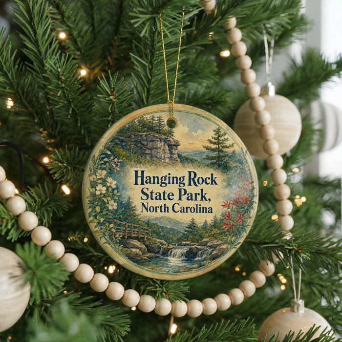 A round ornament hanging on a Christmas tree, featuring a scenic landscape with a waterfall and a bridge.